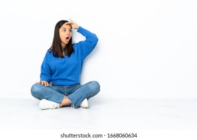 Young mixed race woman sitting on the floor isolated on white background doing surprise gesture while looking to the side - Shutterstock ID 1668060634