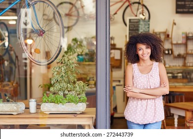 Young Mixed Race Woman Smiling While Standing In The Door Of Her Cafe With Her Arms Folded Proud To Be The Owner Of A Small Business 