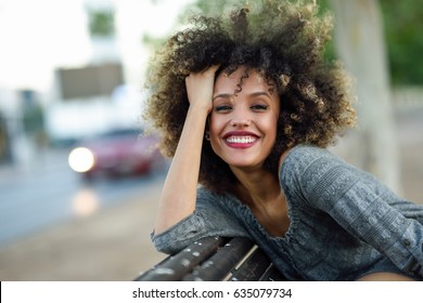 Junge gemischte Frau mit afro-Frisur, die auf urbanem Hintergrund lächelt. Schwarzes Mädchen, das lockere Kleidung trägt.