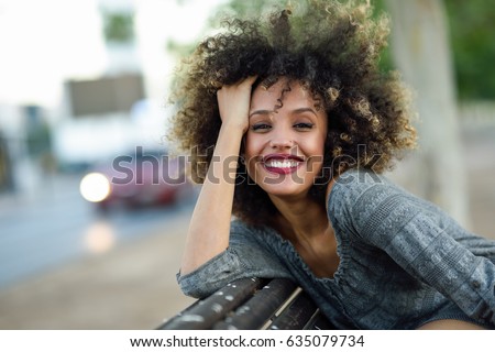 Young mixed woman with afro hairstyle smiling in urban background. Black girl wearing casual clothes.