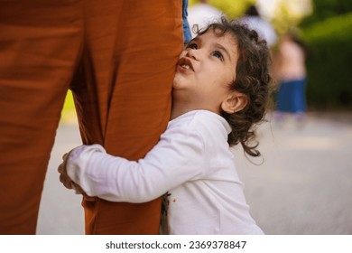 Young Mixed-Ethnicity Girl Embracing Mother's Leg - A 3-year-old girl with curly hair of Italian-Brazilian descent hugs her mother's leg tightly, capturing an intimate and tender moment.