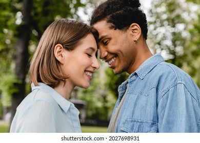 Young Mixed-race Couple Going To Kiss Each Other Embracing Hugging Walking In City Park On Romantic Date Together. Love At First Sight, First Love, True Feelings Relationship Concept