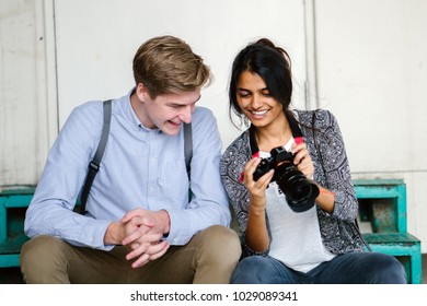 A young mixed-race couple review photographs on a step. They're tourists in Asia and they are both young, attractive and excited. The man is Caucasian and the woman is Indian. They're both smiling.  - Powered by Shutterstock