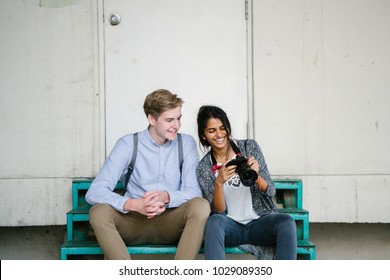 A young mixed-race couple review photographs on a step. They're tourists in Asia and they are both young, attractive and excited. The man is Caucasian and the woman is Indian. They're both smiling.  - Powered by Shutterstock