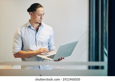 Young Mixed-race Software Developer Testing New Program On Laptop When Standing In Office Room