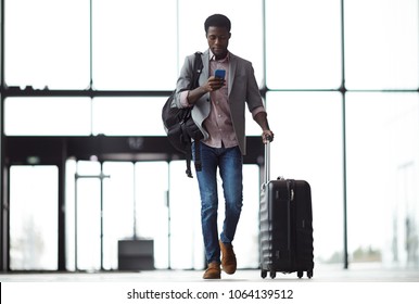 Young mobile traveler with smartphone, backpack and suitcase walking along airport and messaging or looking through online information - Powered by Shutterstock