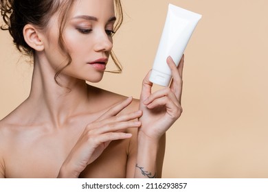 Young model with naked shoulder holding cosmetic lotion isolated on beige
