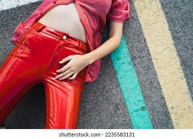 Young model posing for a fashion photoshoot wearing latex pants lying on the floor.