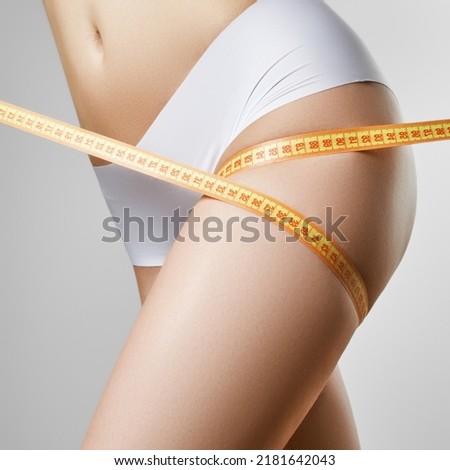 Young model with sports figure measuring her hips. Slim model measuring her hips with centimeter in studio. Photo of beautiful slim body. Woman's shape with clean skin, flat belly