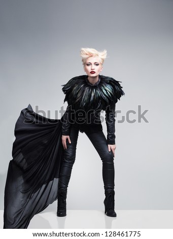 young model wearing leather clothes and feathers posing on  reflective platform