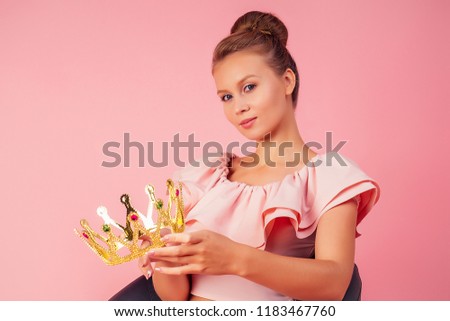 Young model woman in crown in a stylish summer outfit on pink background sitting on chair in studio