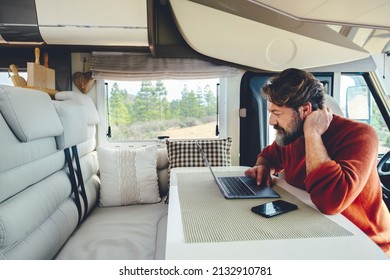 Young Modern Adult Man Work On Laptop Computer In Remote Working And Digital Job Lifestyle Inside A Modern And Connected Camper Van With Nature Woods View Outside The Window. Freedom Lifestyle People