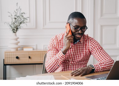 Young Modern African Businessman Talking Via Mobile Phone With Client Or Partner While Working Remotely At Home, Pleased Male Afro American Office Worker Making Call Using Smartphone At Work