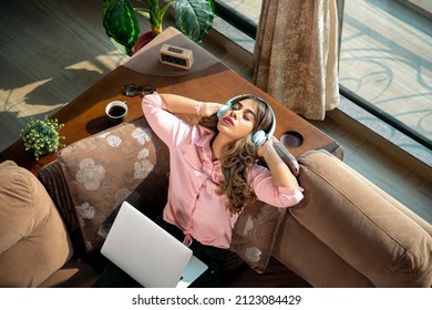 A young modern attractive and beautiful Asian Indian Latina female or woman is taking a break from work and absorbed in listening to music with eyes closed in an apartment or interior house setup. 