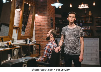 Young modern barber on his workplace with client in hair salon