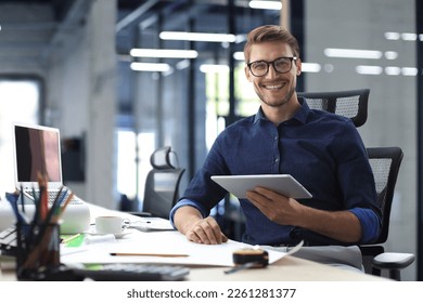 Young modern business man working using digital tablet while sitting in the office - Shutterstock ID 2261281377