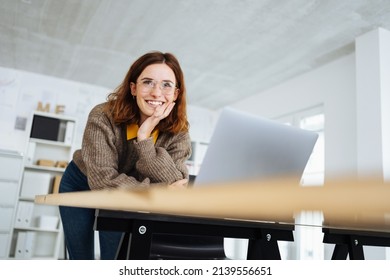 junge, moderne Geschäftsfrau, die sich auf den Schreibtisch stützt und lacht