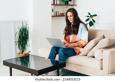 Young Modern Business Woman Sitting At Home On The Sofa Uses A Laptop For Remote Work.