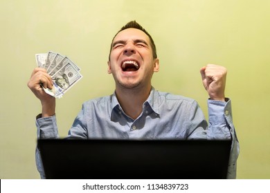 young modern businessman excited with his success while working with his laptop computer. Man shouting for joy, holding the money. 500 dollars in hand. winning the lottery