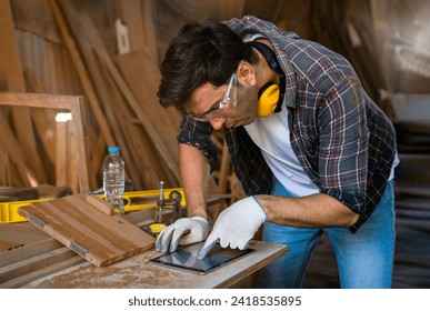 A young modern caucasian craftsman using tablet computer design woodcraft at the carpentry workshop