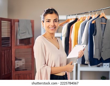 Young Modern Confident Indian Asian Entrepreneur woman or female professional fashion stylist is holding a notebook or a laptop in hand in boutique looking at camera. Self-employment, Startup concept