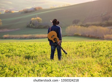 the young modern cowboy with his guitar at the countryside on a sunset evening in the spring season