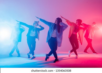 Young modern dancing group of six adult young people practice dancing on colorful background. Fashionably dressed youngsters moving over blurred disco club color lights