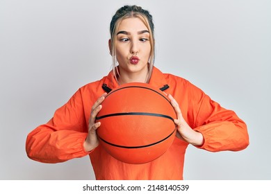 Young modern girl holding basketball ball making fish face with mouth and squinting eyes, crazy and comical. 