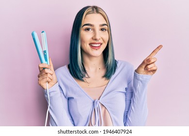 Young Modern Girl Holding Hair Straightener Smiling Happy Pointing With Hand And Finger To The Side 