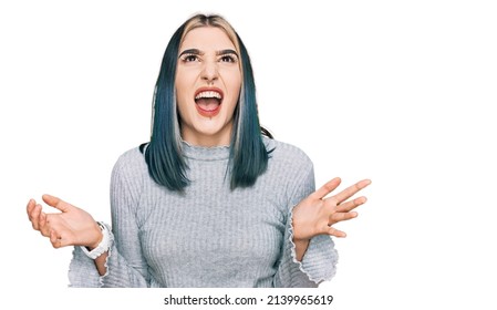 Young modern girl wearing casual sweater crazy and mad shouting and yelling with aggressive expression and arms raised. frustration concept. 