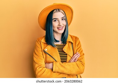 Young modern girl wearing yellow hat and leather jacket happy face smiling with crossed arms looking at the camera. positive person. 