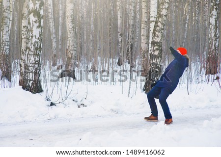 Young modern man slipped and lost his balance during a walk on a birch grove in winter. Freeze frame while jumping and waving his hands before falling to the snow.