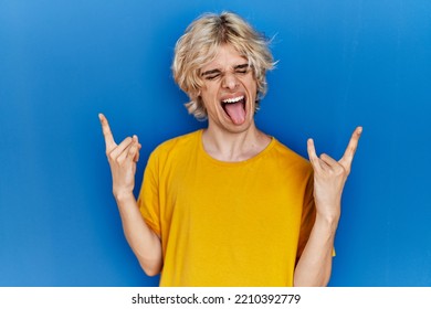 Young Modern Man Standing Over Blue Background Shouting With Crazy Expression Doing Rock Symbol With Hands Up. Music Star. Heavy Concept. 