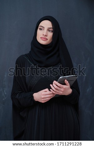 young modern muslim business woman holding tablet computer wearing hijab clothes in front of black chalkboard