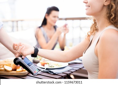 Young modern woman with smartwatch keeping her wrist over electronic payment machine while paying for food - Powered by Shutterstock