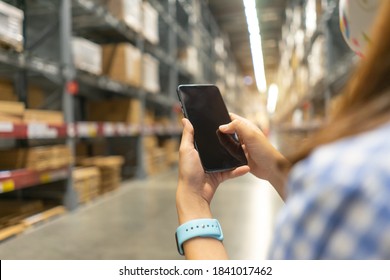 Young Modern Woman Using Touch Screen Mobile Phone In Warehouse Storage.
