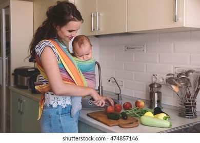 Young Mom Cooking In The Kitchen With The Little Baby In A Sling. Vegetarian Healthy Food. Healthy Food Breastfeeding Mothers.