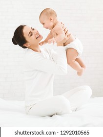 Young Mom Enjoying Time With Her Newborn Baby, Holding Her Happy Son In Air