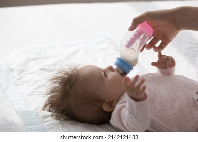 Young Mom Feeding Sweet Infant Baby, Giving Formula. Sweet Few Month Kid Resting On Back On Bed, Drinking Breast Milk From Bottle. Childhood, Childcare, Postnatal Care, Motherhood Concept