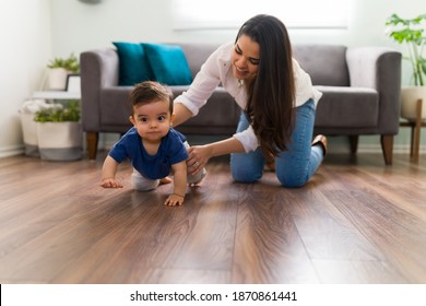 Young Mom Helping Baby Boy Crawl On Living Room Floor