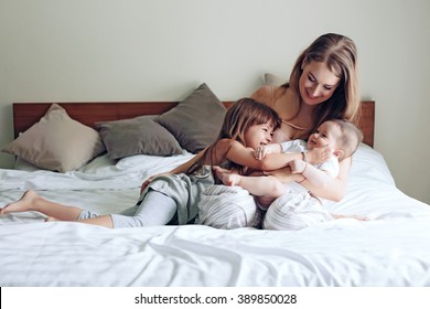 Young mom with her 5 years old daughter and 4 months old baby dressed in pajamas are relaxing and playing in the bed at the weekend together, lazy morning