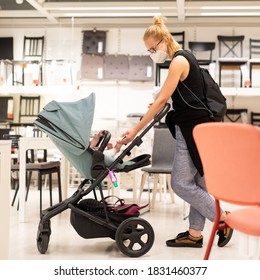 Young Mom With Newborn In Stroller Shopping At Retail Furniture And Home Accessories Store Wearing Protective Medical Face Mask To Prevent Spreading Of Corona Virus. New Normal During Covid Epidemic.