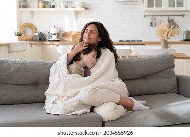 Young Mom Sit On Cozy Couch Relax With Preschool Child Covered With Blanket Bonding With Kid On Weekend Morning At Home. Loving Mother Single Parent Wrapping Embrace Small Son On Sofa In Living Room