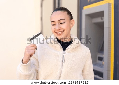 Young moroccan girl holding a credit card at outdoors with happy expression