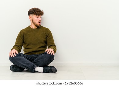 Young Moroccan man sitting on the floor isolated on white background being shocked because of something she has seen.