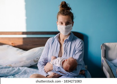 Young mother after giving birth will rock her newborn at home in the bedroom on the bed. Maternity in the COVID-19 pandemic new normal. Postpartum period. Mom in a protective medical mask. Quarantine