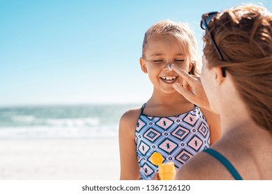 Young mother applying protective sunscreen on daughter nose at beach. Woman hand putting sun lotion on child face. Cute little girl with sunblock at seaside with copy space. - Shutterstock ID 1367126120