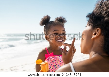 Young mother applying protective sunscreen on daughter nose at beach with copy space. Black woman hand putting sun lotion on female child face. African american cute little girl with sunblock cream. ストックフォト © 