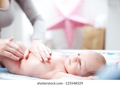 Young Mother Applying Talc To An Adorable Tiny Newborn Baby While It Lies On Its Back In The Nursery Having A Nappy Change