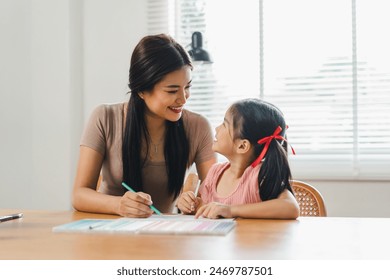 Young mother assists her daughter with coloring activities at a home desk during daytime - Powered by Shutterstock